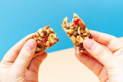 Female hands holding a broken piece of protein bar on blue and brown background.