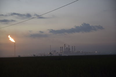 Fire emitting from smoke stack at industrial site against sky