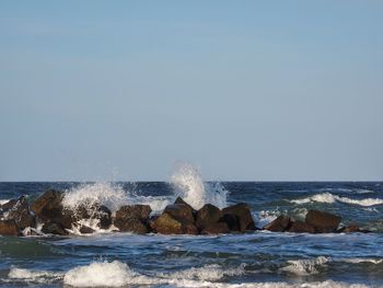 Sea waves splashing on rocks against clear sky