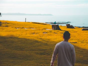 Rear view of young man standing on field against sea