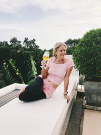 Woman having wine while sitting on wall against sky