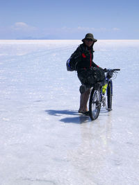 Portrait of mid adult man with bicycle standing at salar de uyuni against blue sky