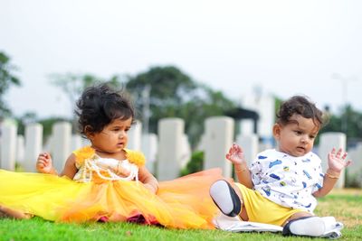 Cute siblings sitting on grassy field at park