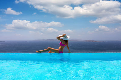 Woman sitting at infinity pool against sea