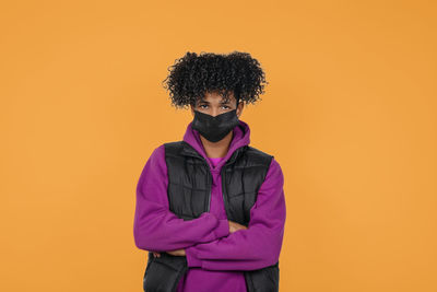 Portrait of young man wearing mask standing against orange background