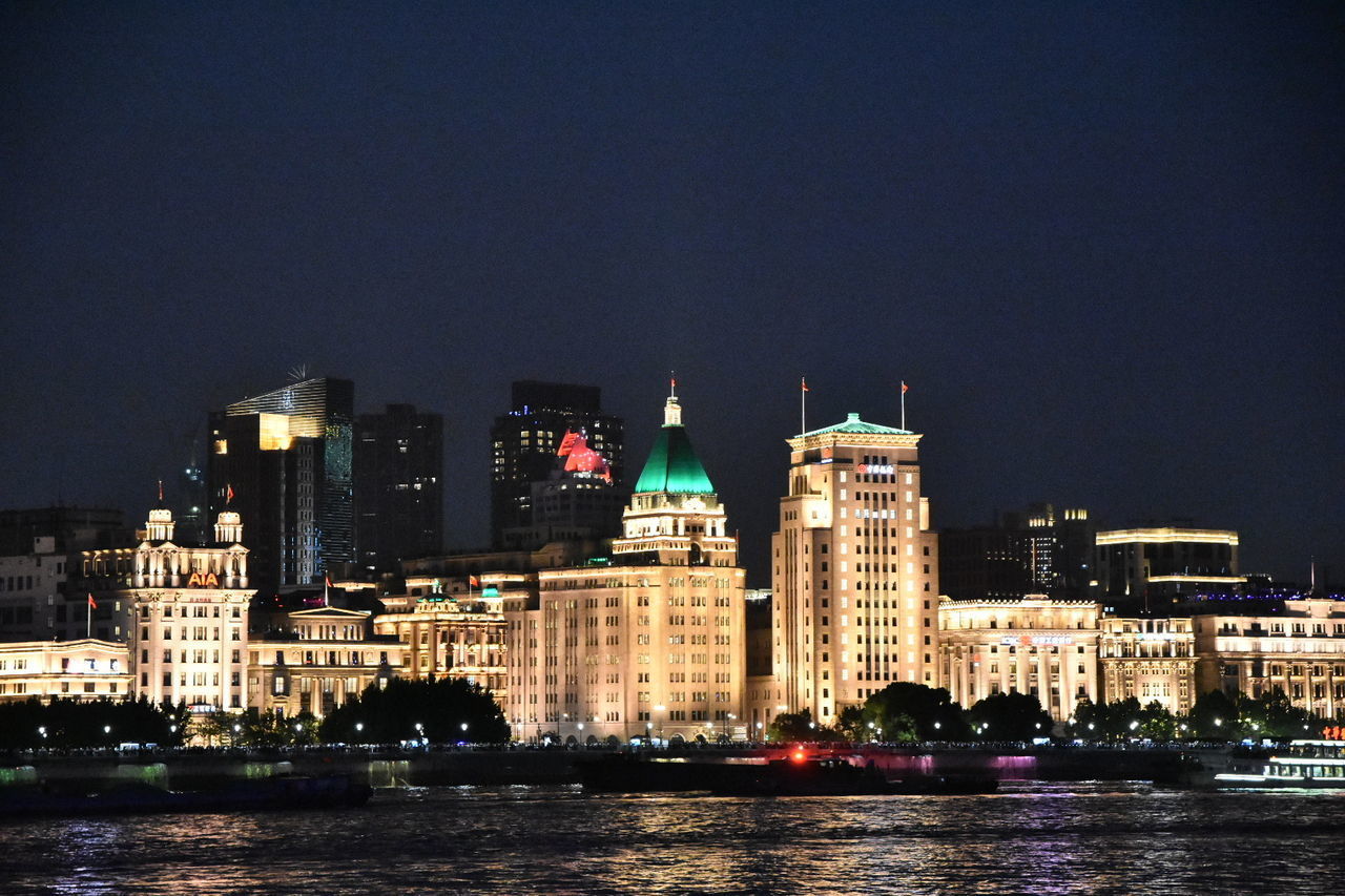 ILLUMINATED BUILDINGS BY RIVER AGAINST SKY