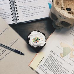 High angle view of cupcake and human skull amidst books