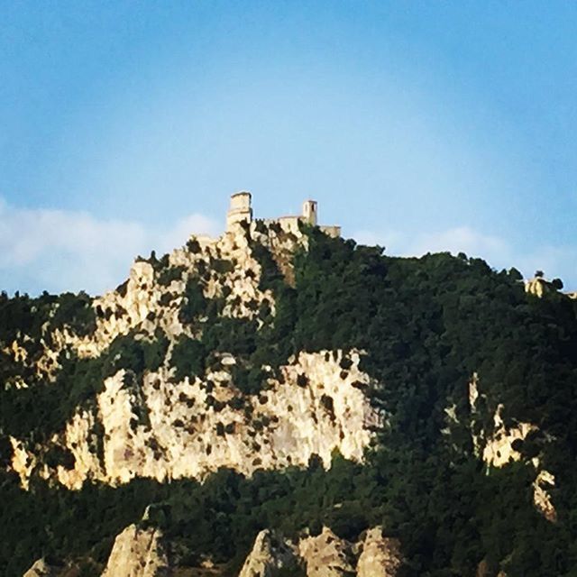 low angle view, clear sky, blue, architecture, built structure, building exterior, mountain, sky, history, copy space, rock - object, rock formation, stone wall, old ruin, sunlight, day, nature, the past, hill, ancient