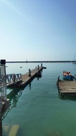 Fishing boats moored in sea against clear blue sky