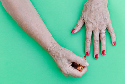 Elderly painting her nails in red with a green background, flat on top