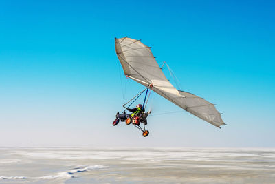 Man paragliding over sea against blue sky