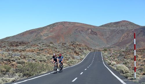 Men riding bicycle on road against clear sky