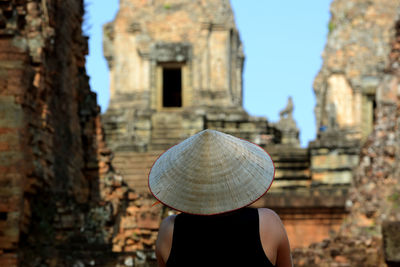 Rear view of person wearing asian style conical hat by historical building