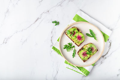 Homemade toasts with organic watemelon radish, avocado and flex seeds on white marble background