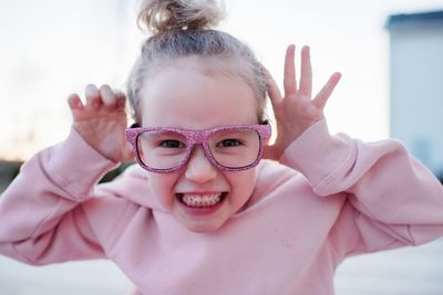 Portrait of a young girl pulling funny faces with pink sparkly glasses