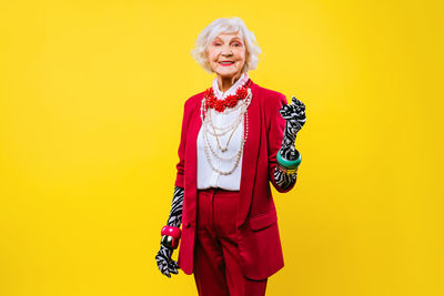 Portrait of senior woman standing against yellow background