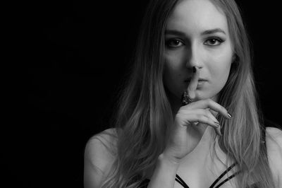 Portrait of beautiful young woman with finger on lips against black background