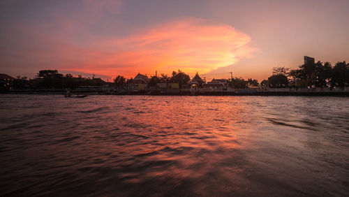 Silhouette city by sea against sky during sunset