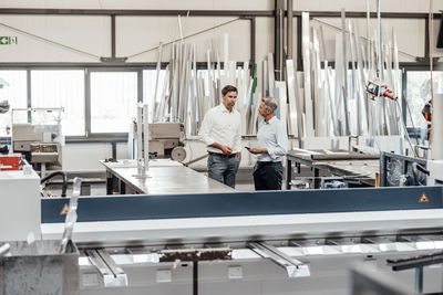 Male mature engineers discussing while standing in factory