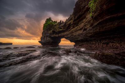 Rock formation in sea against sky during sunset