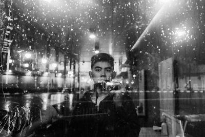 Portrait of man photographing through wet window