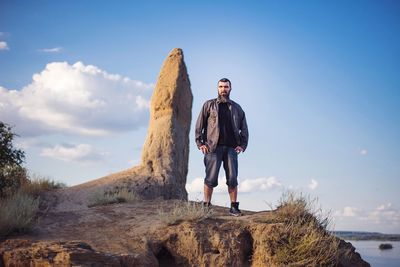 Full length of young man standing on rock against sky