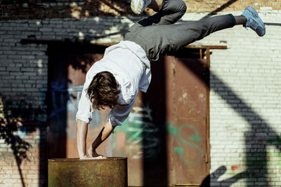 Full length of man doing stunt on container against wall