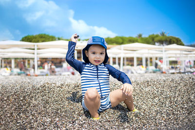 Toddler boy in a swimming suit plays with pebbles on the seashore in hotel