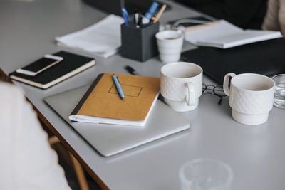Book kept over laptop near coffee cups on table in office