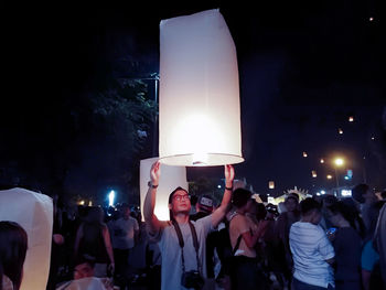 Group of people at illuminated street against sky at night