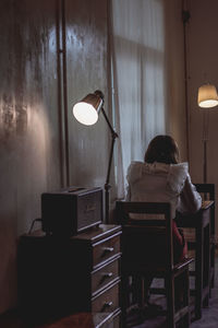 Rear view of woman sitting on table in illuminated room