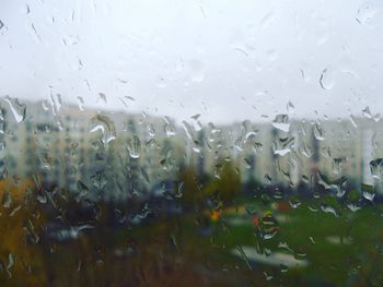 Building against sky seen through wet glass window during rainy season