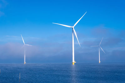 Wind turbines in sea against blue sky