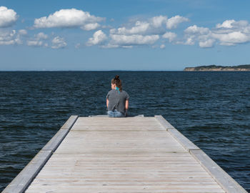 Woman sitting on jetty against sea