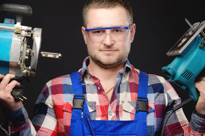 Portrait of young man holding eyeglasses against black background