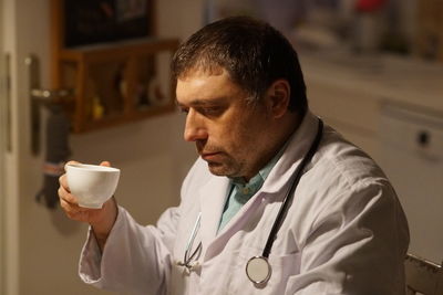 Side view of thoughtful mature doctor with coffee sitting in hospital