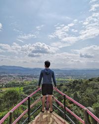 Rear view of man standing on railing against sky