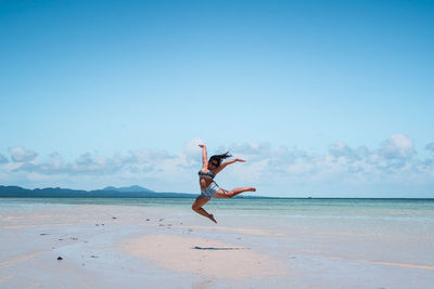 Young woman jumping at beach against blue sky