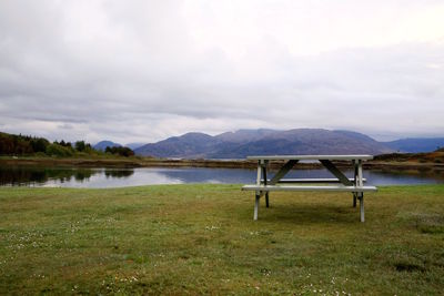 Empty chairs by lake against sky