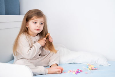 Cute girl combing hair sitting on bed