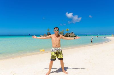 Full length of shirtless man standing at beach against sky