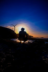 Rear view of silhouette man on beach against sky during sunset