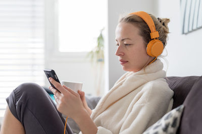 Mid adult woman listening music sitting on sofa at home