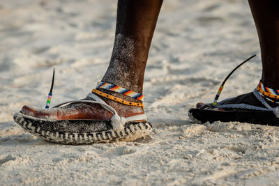 Tribal masai legs with a colorful bracelet and sandals made of car tires on the sand beach, close up