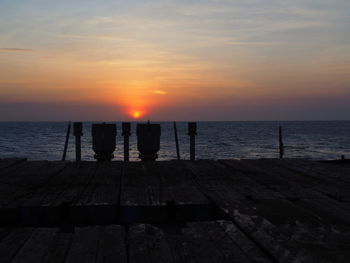 Silhouette men standing by sea against sky during sunset