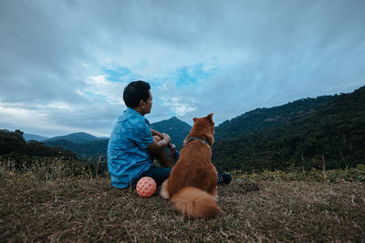 Rear view of man with dog sitting on land