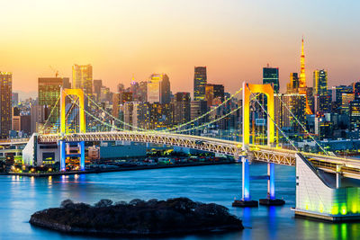 Illuminated bridge and buildings against sky during sunset