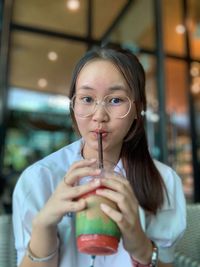 Portrait of young woman drinking smoothie while sitting in cafe