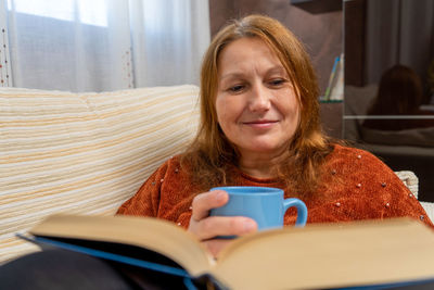 Mature woman drinking coffee while reading book at home