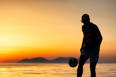 Silhouette man standing on beach against sky during sunset